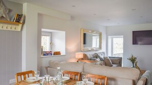 Un comedor con una mesa de madera dispuesta para cuatro, un sofá al fondo y un espejo en la pared.