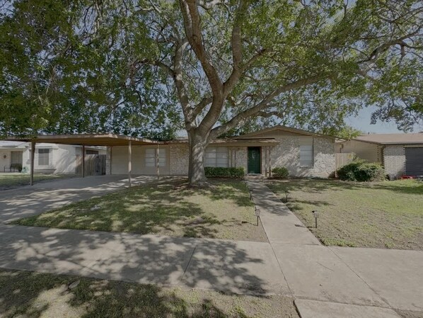 Uma casa de dois andares com varanda coberta, quintal frontal e entrada para carros.