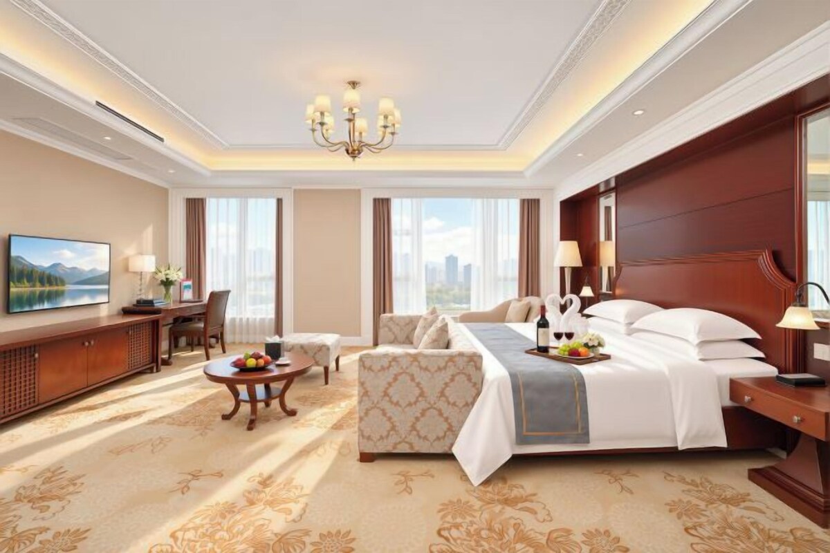 A hotel room with a large bed, a sofa, a desk, and a television.
