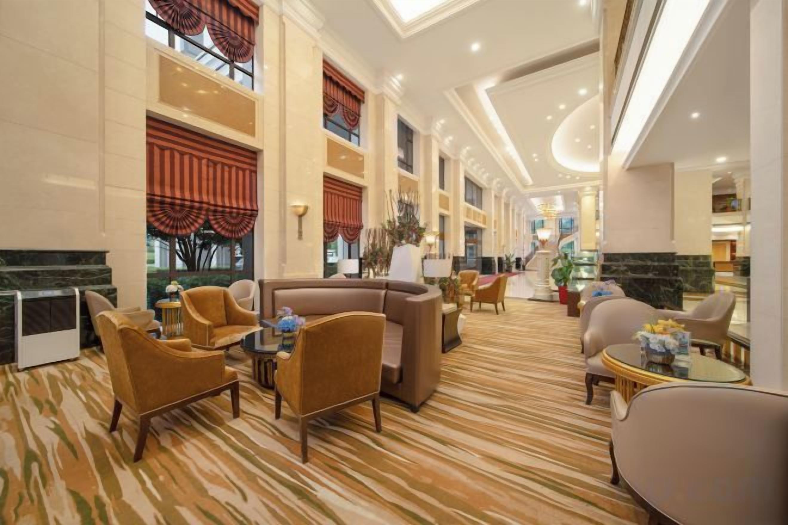 A hotel lobby with a high ceiling, a marble reception desk, and a seating area with sofas and armchairs.