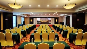 A conference room with rows of yellow chairs and green tables, equipped with water bottles. - Garden Hotel (Jinzhai)