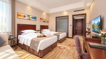 Habitación de hotel con dos camas, un escritorio, un televisor y obras de arte en las paredes.