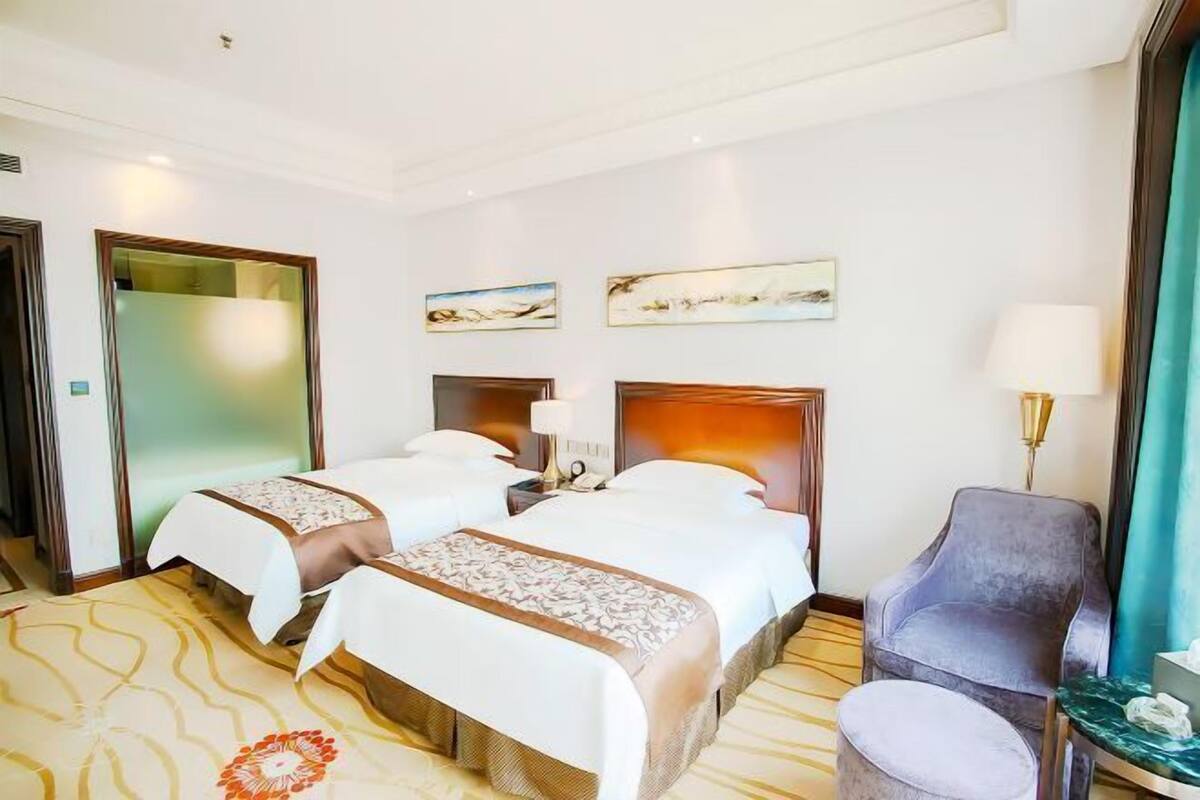 A hotel room with two beds, a chair, a small table, and artwork on the wall.