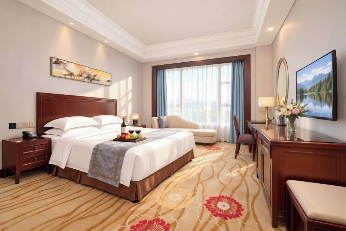 A hotel room with a large bed, a desk, a chair, and a view of the outdoors.