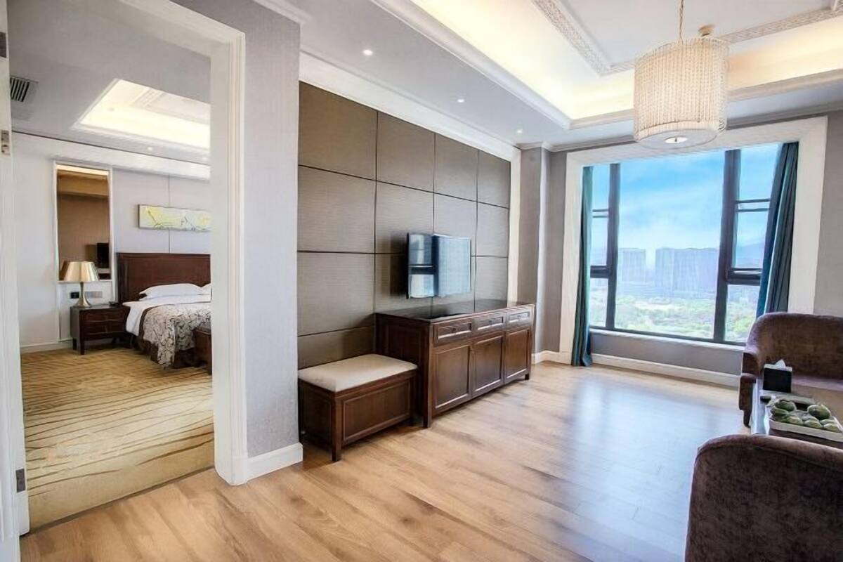 A modern hotel room with a large bed, a TV, a desk, and a view of the city.