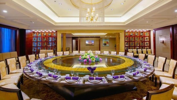 A conference room with a round glass table, surrounded by chairs, and a chandelier above. - Garden Hotel (Jinzhai)