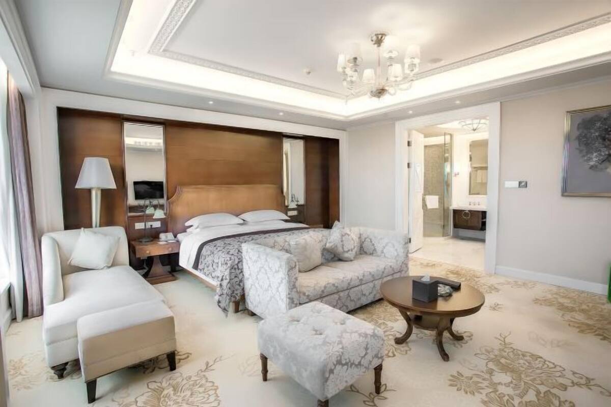 A hotel room with a bed, a sofa, a chair, a small table, and a mirror.