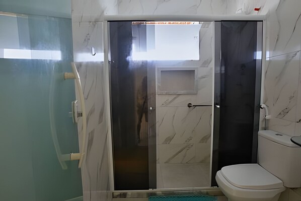 A bathroom with a glass-enclosed shower, a toilet, and a marble wall.