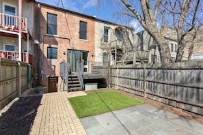 A residential building with a brick exterior, a wooden deck, a fenced backyard, and a small lawn area. - Modern 4 Bed, 3.5 Bath Home | Near Sox & McCormick (Chicago)