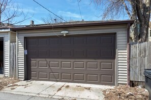 A garage with a brown door, a wooden fence, and a tree in the background.