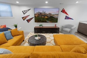 A living room with mustard-colored sofas, a round coffee table, and a flat-screen TV mounted on the wall. - Modern 4 Bed, 3.5 Bath Home | Near Sox & McCormick (Chicago)