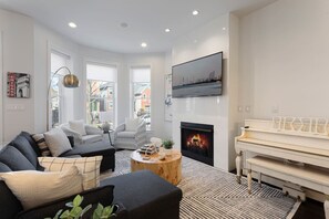 A modern living room with a fireplace, a piano, and a large window offering a city view.