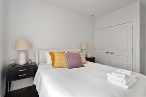 A neatly made bed with white linens, a black nightstand with a lamp, and a white door. - Modern 4 Bed, 3.5 Bath Home | Near Sox & McCormick (Chicago)