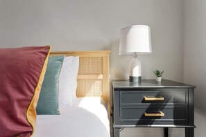 A neatly made bed with a wooden headboard, a bedside table with a lamp, and a small potted plant.