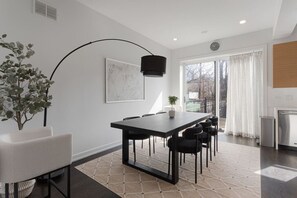 A modern dining area with a long table, chairs, a floor lamp, and a potted plant. - Modern 4 Bed, 3.5 Bath Home | Near Sox & McCormick (Chicago)