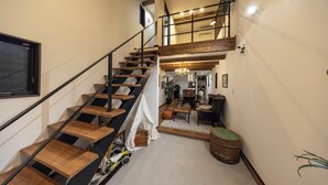 Un espace intérieur à plusieurs niveaux, avec un escalier en bois, un coin jeux équipé d’un tricycle, et un espace détente avec une table et des chaises.