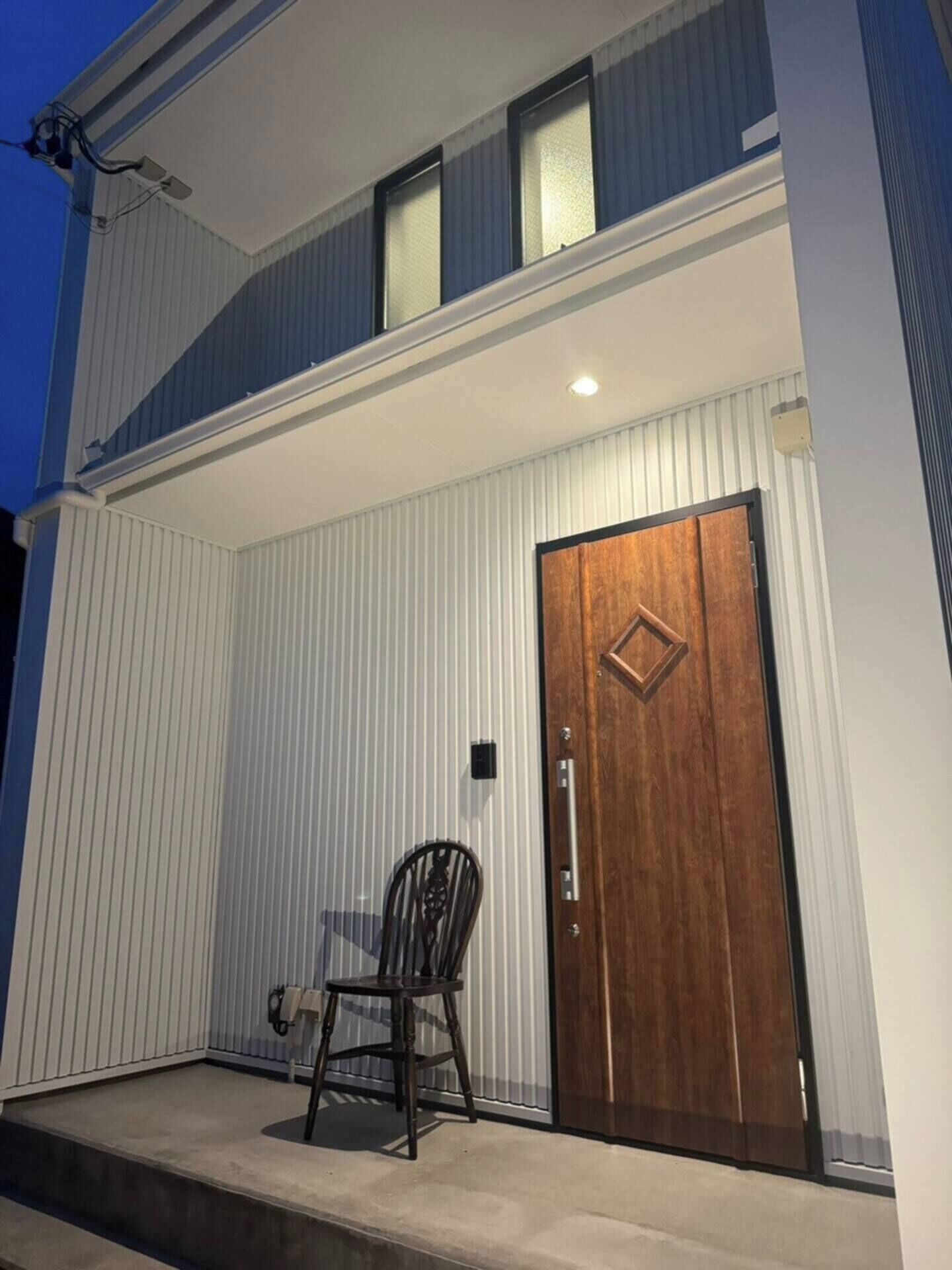 Un edificio moderno de dos pisos con una puerta delantera de madera y una silla afuera.
