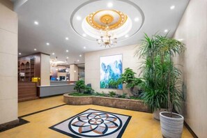 Un vestíbulo de hotel con mostrador de recepción, un candelabro y plantas en macetas.