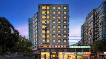 A multi-story hotel with a modern facade, illuminated windows, and a ground-level commercial area with various shops.