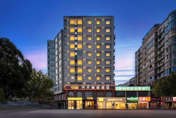 Un hotel de varios pisos con una fachada moderna, ventanas iluminadas y una zona comercial en la planta baja con diversas tiendas.