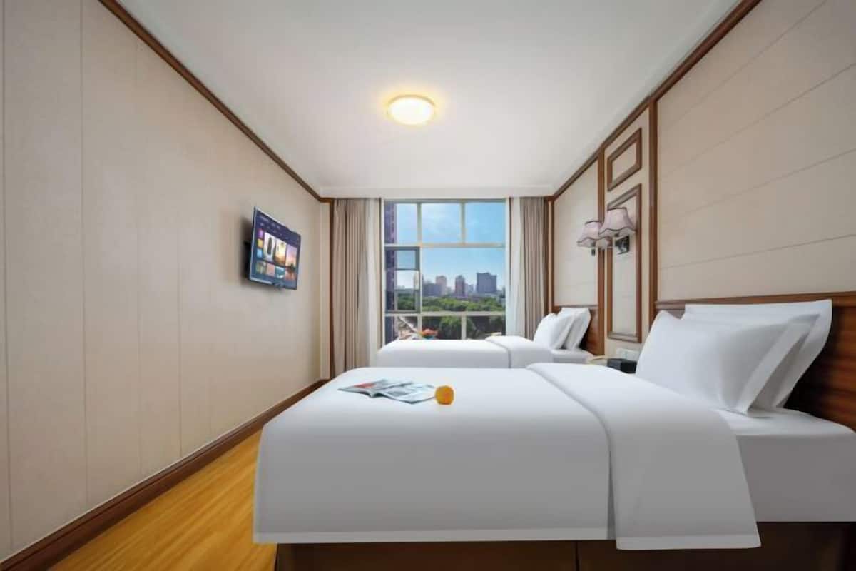 Habitación de hotel con cama, ventana con vista a la ciudad, televisor montado en la pared y luz de techo.
