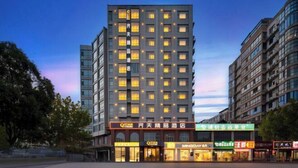 A multi-story hotel with illuminated windows and a variety of storefronts in front.