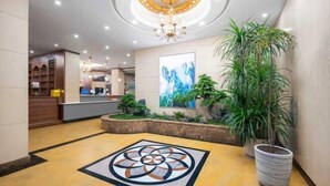 A hotel lobby with a central chandelier, a reception desk, a large abstract painting, and a potted plant.