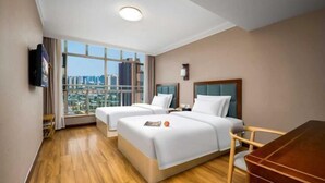 A hotel room with two beds, a wooden floor, a city view, a desk, and a chair.