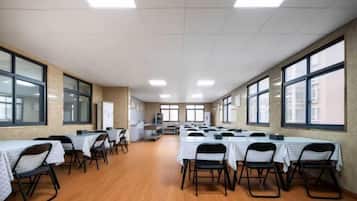 Een vergaderzaal met tafels, stoelen, grote ramen en een hoge plafond.