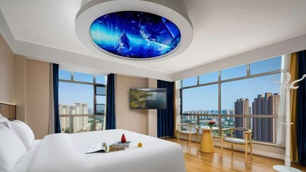 A modern hotel room with a large bed, a ceiling mural, a TV, and a city view.
