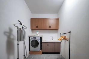 A laundry area with a washing machine, a drying rack, and wooden cabinets. - Qitian Boutique Hotel (Shangqiu)