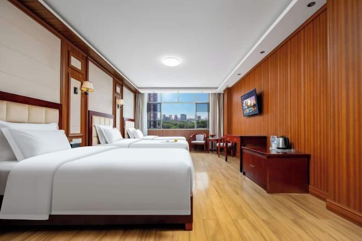 Habitación de hotel con dos camas, un escritorio, una silla, un televisor y una ventana con vistas a la ciudad.