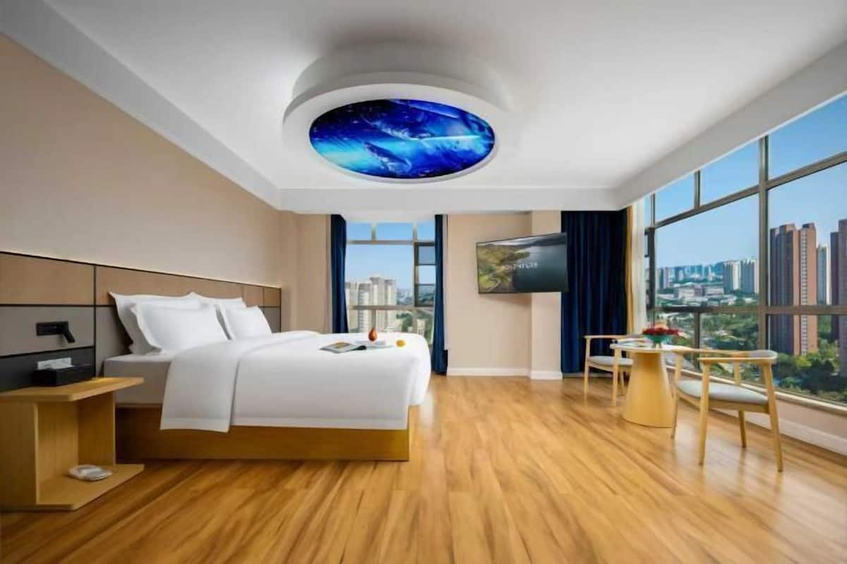 Una habitación de hotel moderna con una cama grande, televisión, zona de comedor y vistas a la ciudad.