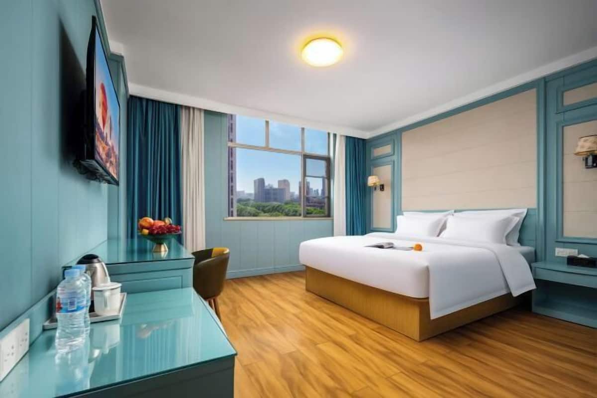 Habitación de hotel con cama, escritorio, silla, televisor y ventana con vista a la ciudad.