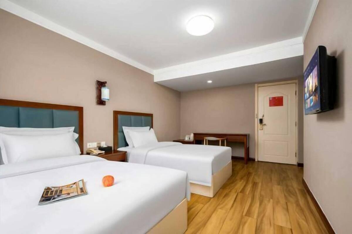 Habitación de hotel con dos camas, un escritorio, un televisor y una puerta.