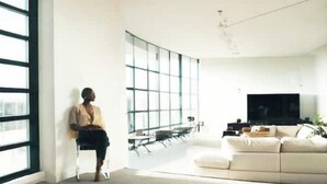 A modern living room with large windows, a sofa, a television, and a dining area.