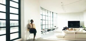 Uma sala de estar moderna com janelas amplas, um sofá, uma televisão e um espaço para refeições.