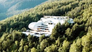 A modern, multi-story building nestled among dense forested hills.
