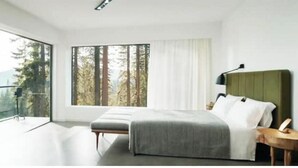 A modern bedroom with a large window, a bed, a bedside table, and a view of trees.