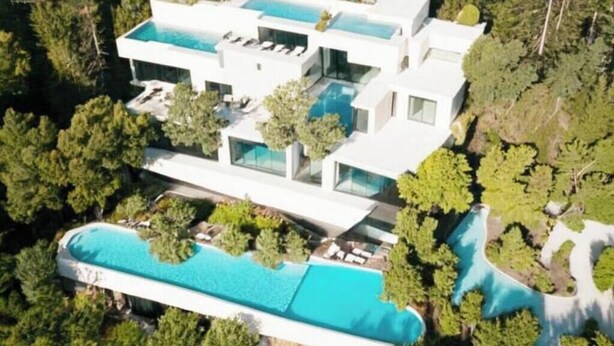 A modern multi-story house with a large swimming pool and lush greenery.