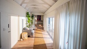 A hallway with a wooden floor, white walls, a sofa, a large plant, and a staircase leading to another room.