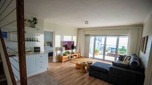 A spacious living area with a sofa, wooden flooring, a dining table, and a kitchen area visible through an open door.