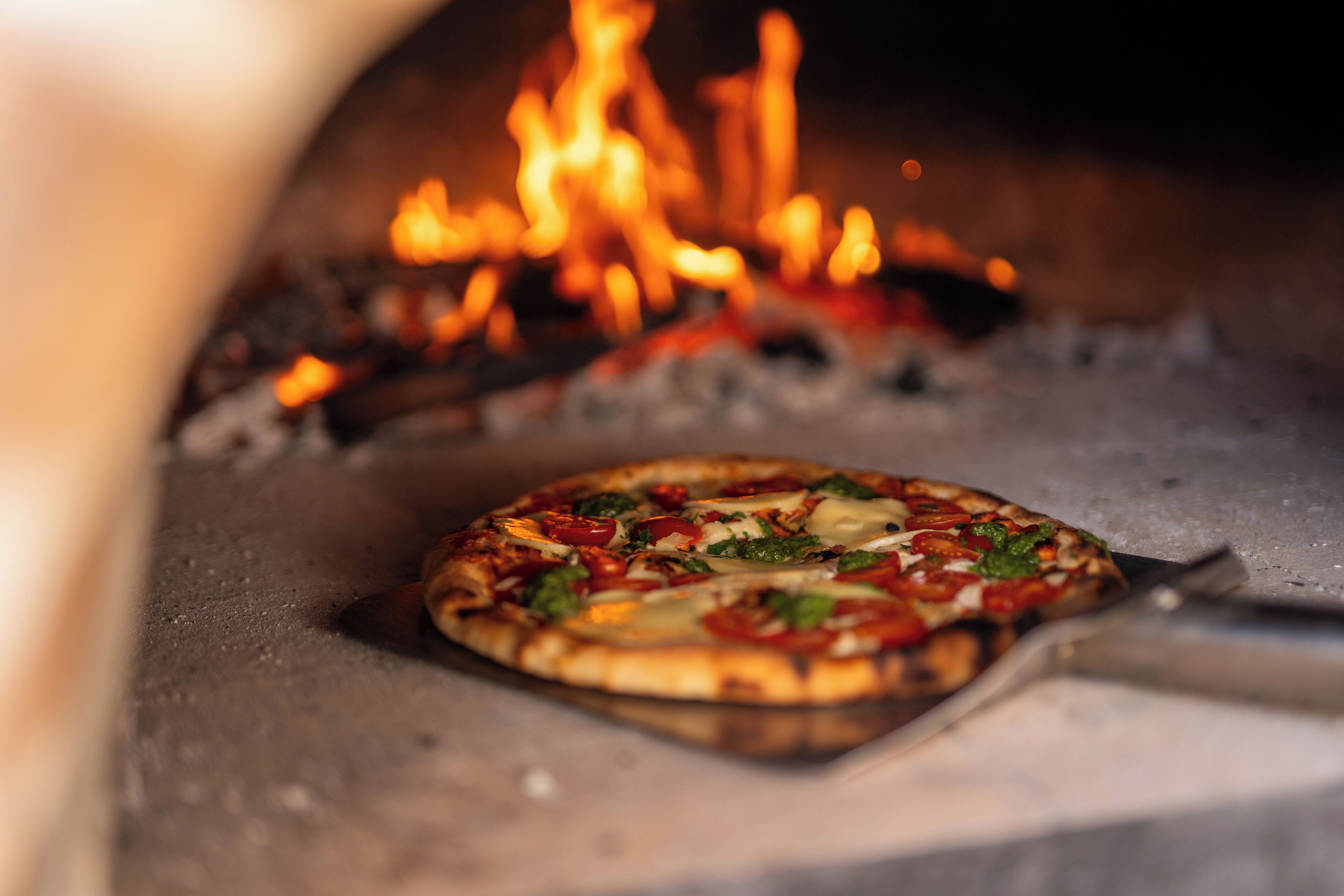 A pizza inside a wood-fired oven with visible flames.