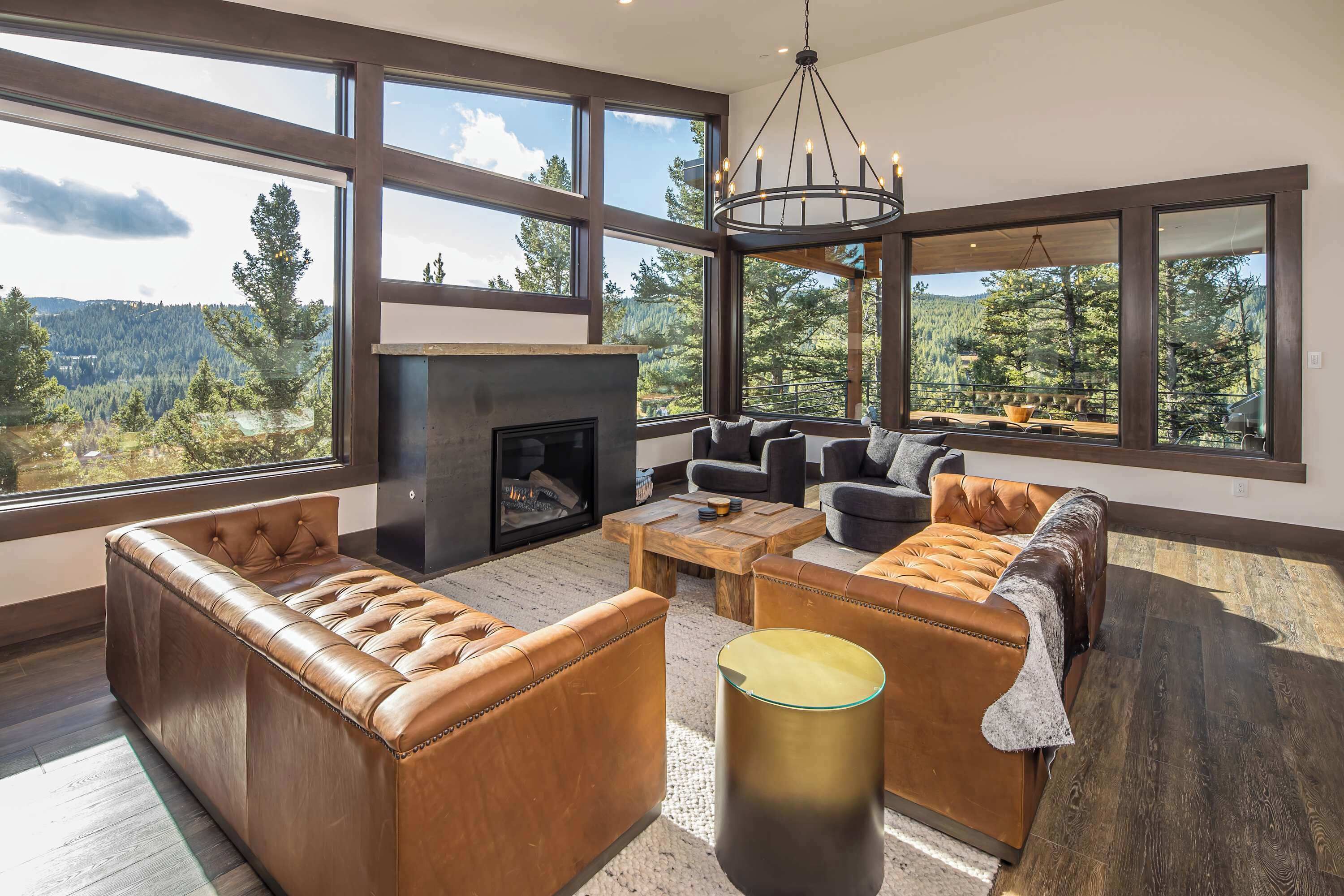 A spacious living room with leather sofas, a fireplace, and large windows offering a mountain view.