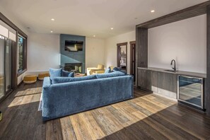 A modern living room with a blue sofa, a fireplace, and a kitchen area with a sink.