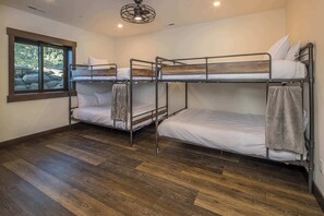 Une pièce avec trois lits superposés, un plancher en bois, une fenêtre donnant sur des rochers et un ventilateur de plafond.