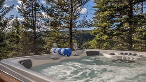 Un jacuzzi con una copa de vino y una toalla, rodeado de árboles y un cielo despejado.