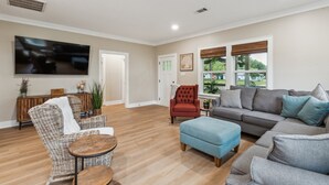 A spacious living room with a large flat-screen TV, comfortable seating, and a view of the outdoors.
