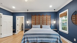 A bedroom with a bed, a wooden headboard, a window with a view, and a door.