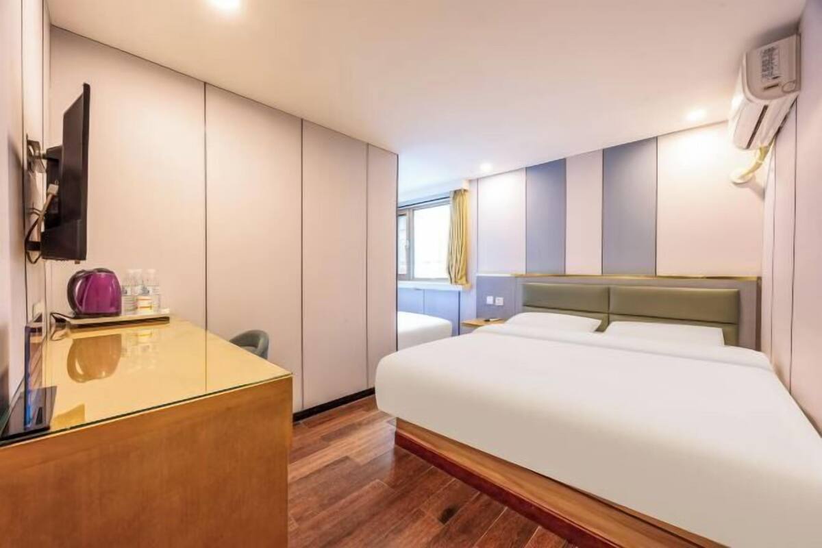 A modern hotel room with a large bed, a desk, a flat-screen TV, and a window with curtains.